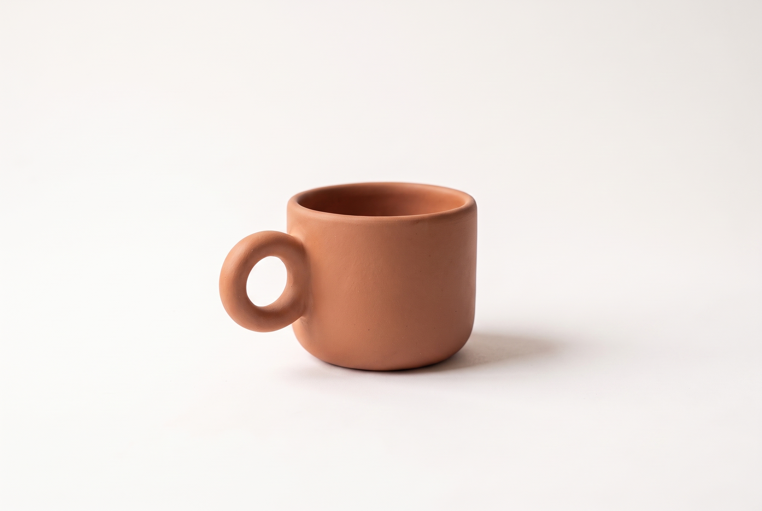 Terracotta ceramic espresso cup in a centered editorial ecommerce product photograph on a warm white studio background