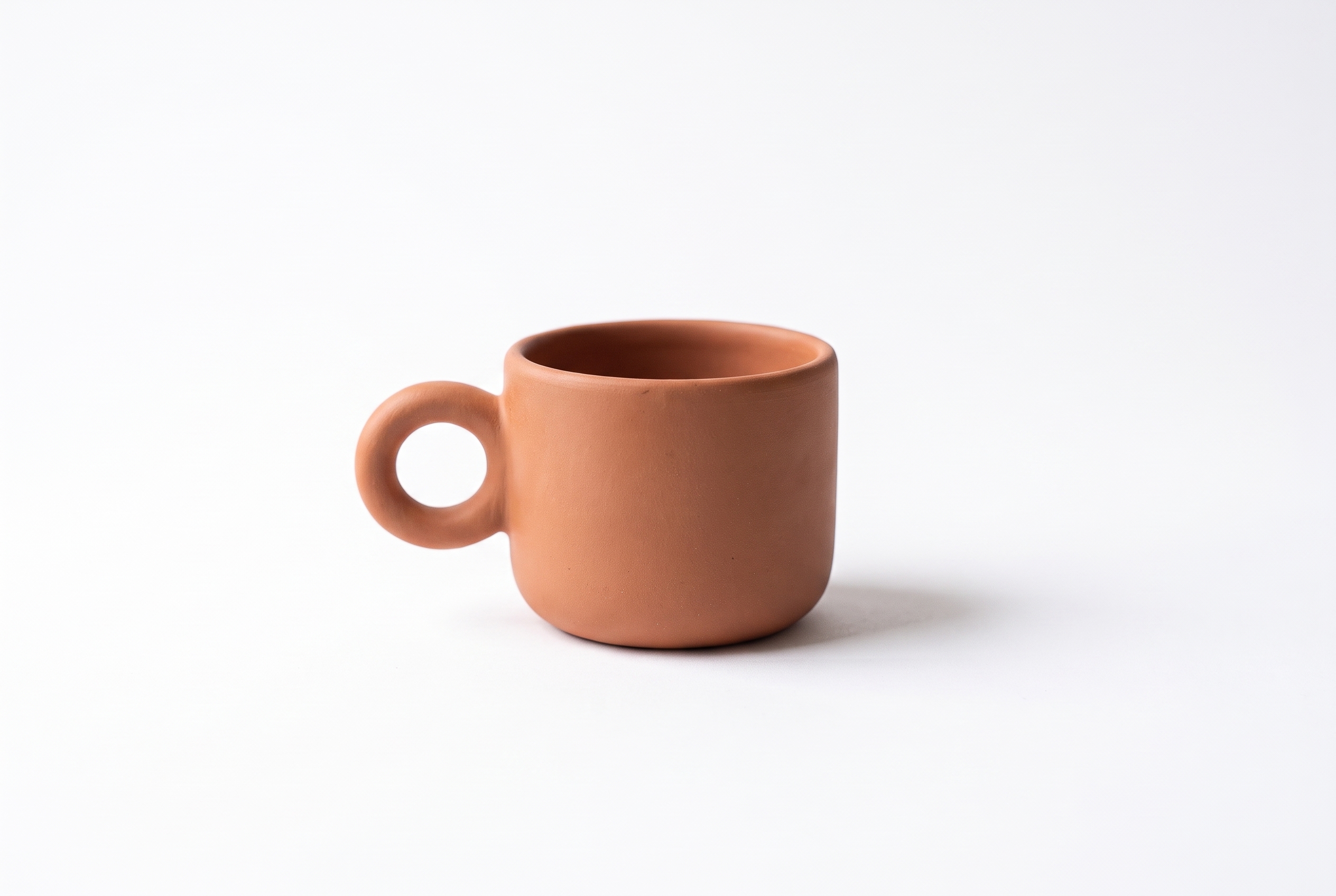 Terracotta ceramic espresso cup centered on a clean white background with a soft shadow